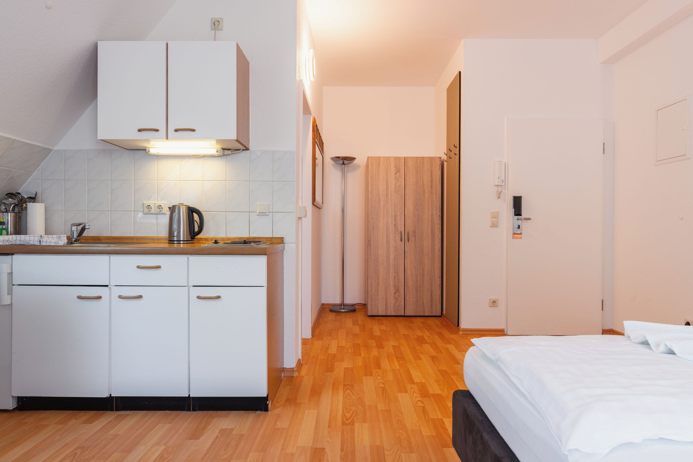 Quarto de hotel compacto com cozinha compacta, uma cama e guarda-roupa de madeira.
