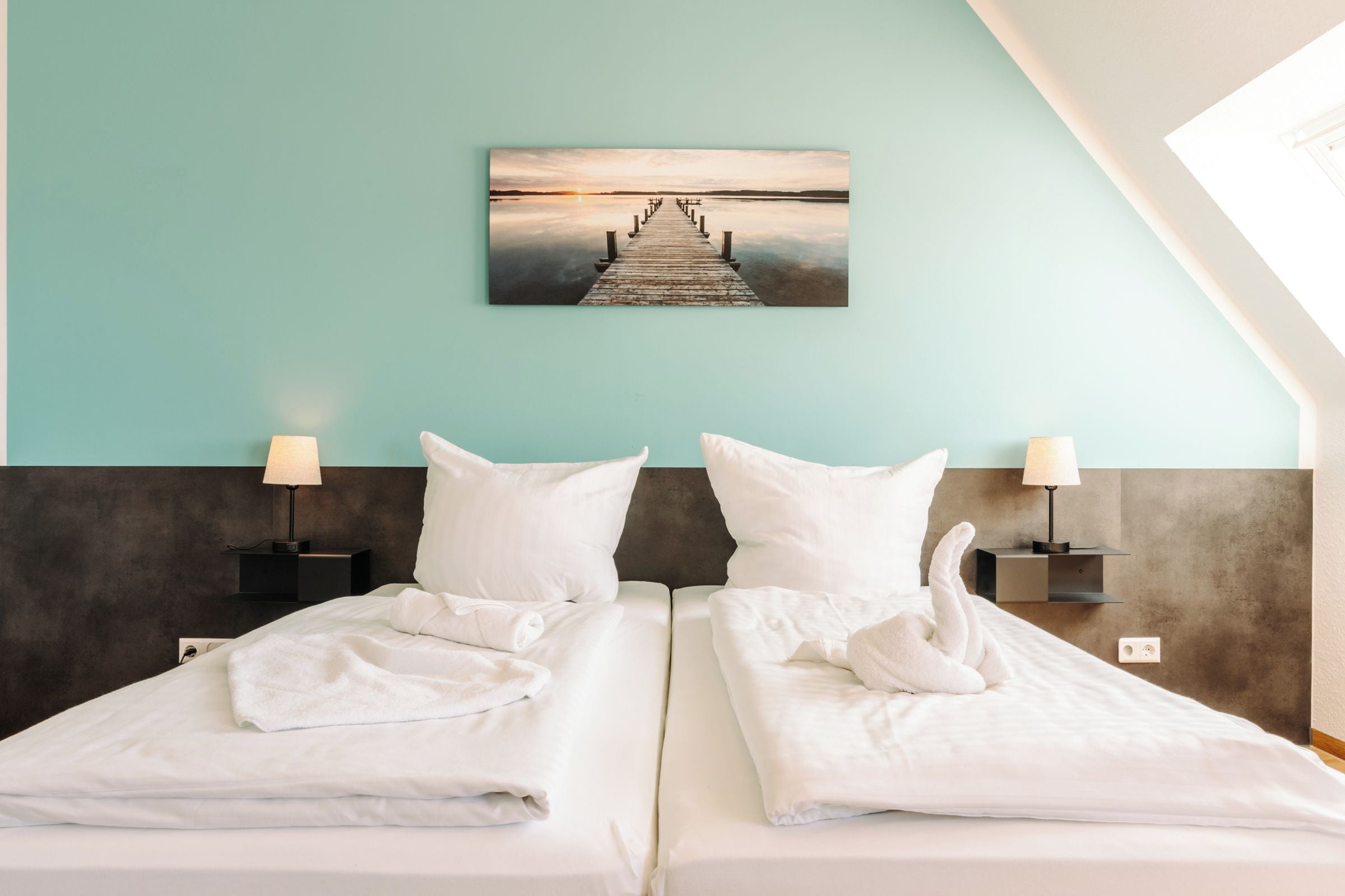 Habitación de hotel con dos camas, un cuadro de un muelle y vista al mar.