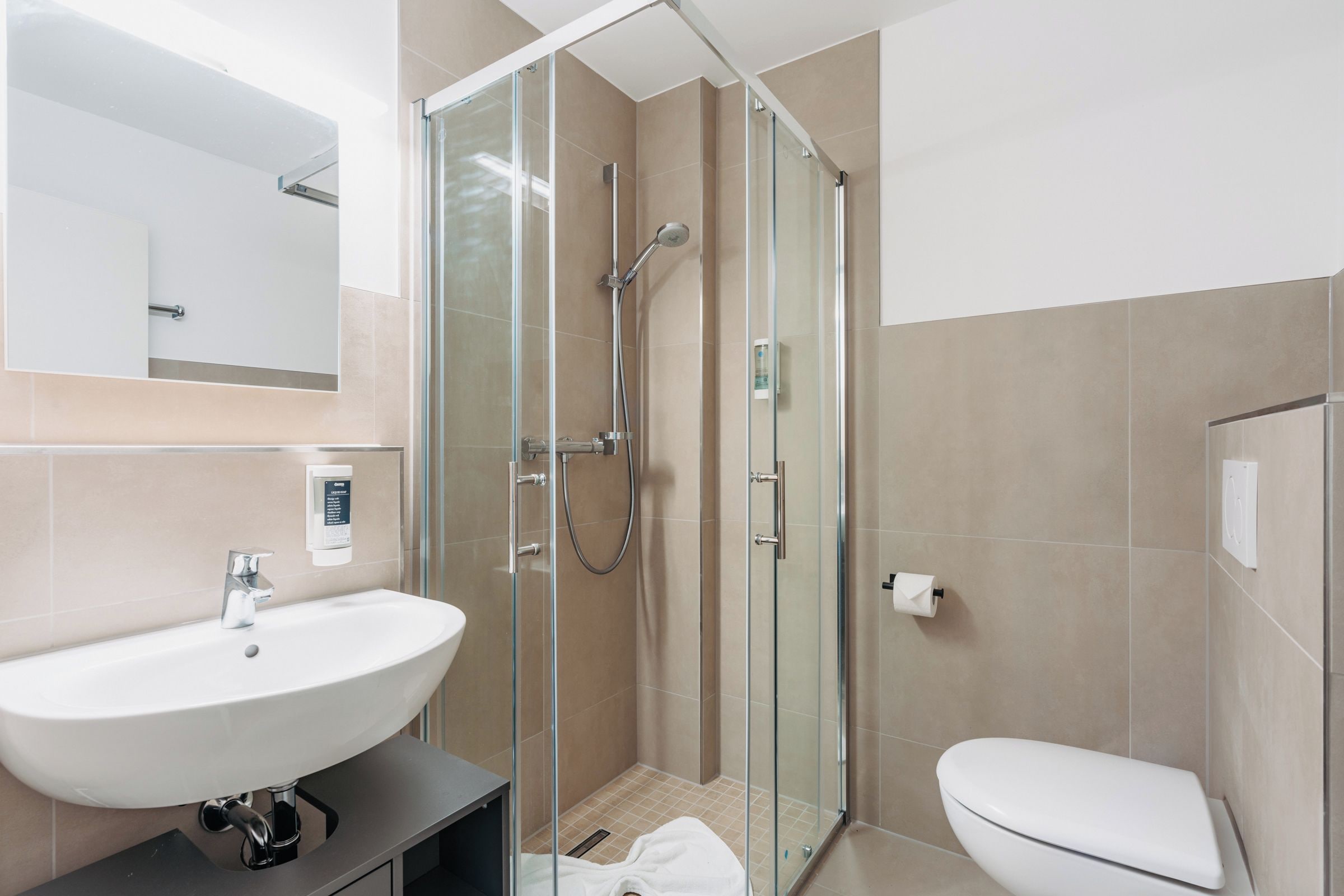 Ein modernes Badezimmer mit einer gläsernen Duschkabine, einem weißen Waschbecken und einer Toilette.