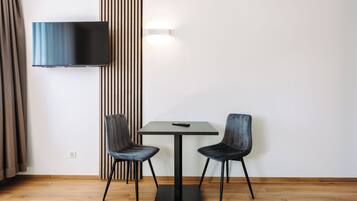 A modern room with a flat-screen TV mounted on the wall, two chairs around a small table, and a wooden floor.