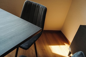 Un coin de pièce avec un plancher en bois, une table de couleur sombre et une chaise.
