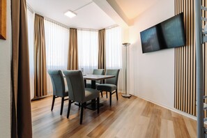 Un comedor moderno con suelo de madera, una mesa, cuatro sillas y un televisor de pantalla plana montado en la pared.