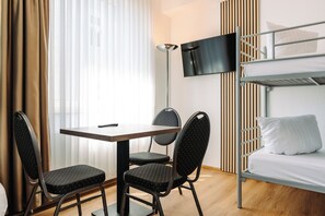 Habitación de hotel con literas, un escritorio con dos sillas, un televisor y una ventana con cortinas.