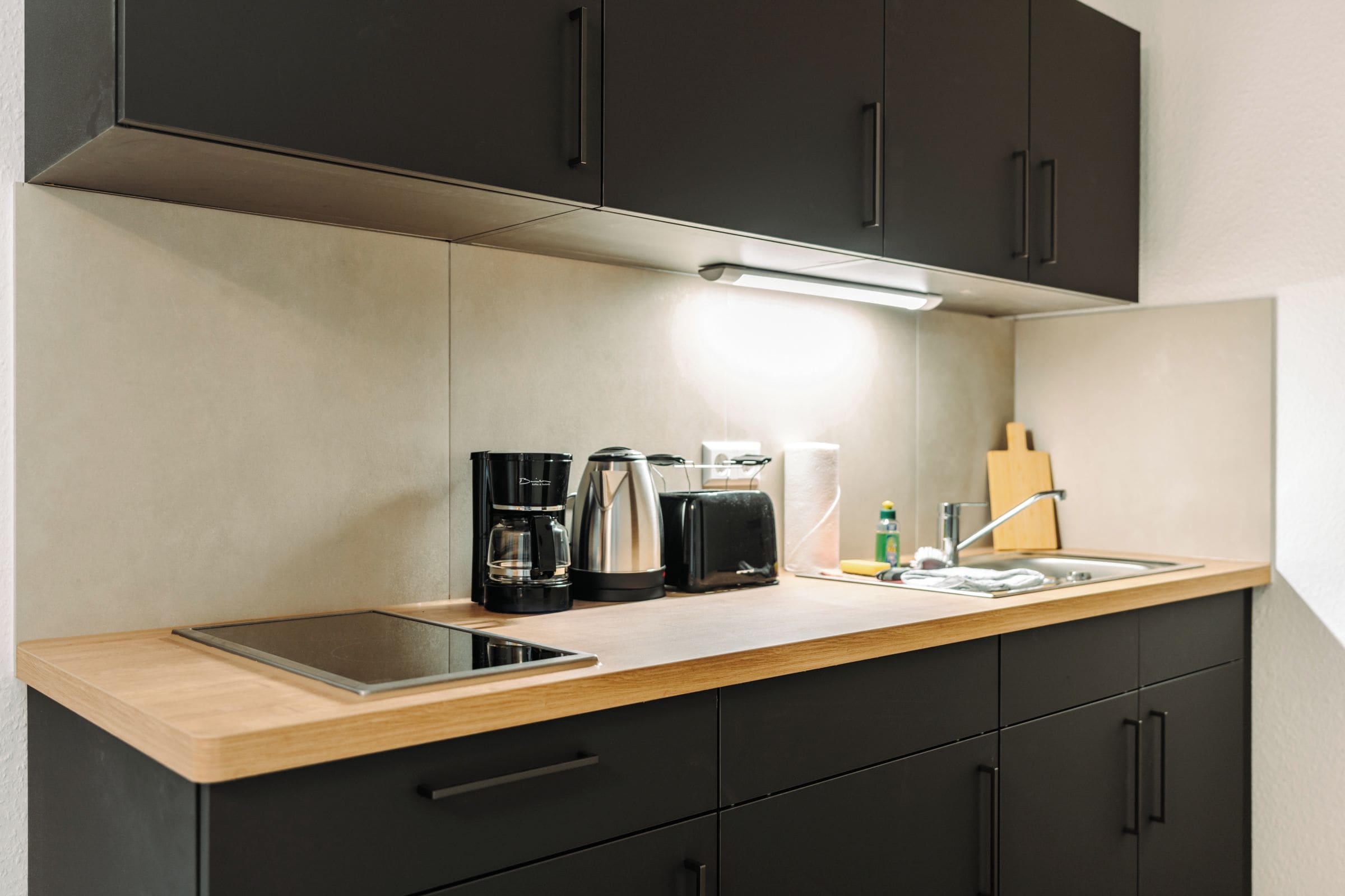 A modern kitchen with a wooden countertop, black cabinets, a built-in oven, and a coffee maker.