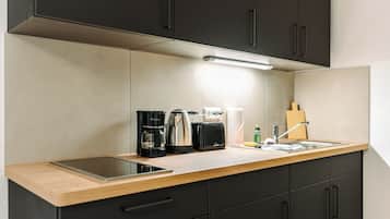 A modern kitchen with a wooden countertop, black cabinets, a built-in oven, and a coffee maker.