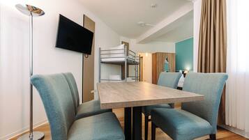 Una habitación de hotel moderna con una cama litera, un televisor de pantalla plana, una mesa de comedor con sillas y una lámpara de pie.