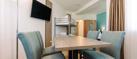 Een moderne hotelkamer met een stapelbed, een flatscreen televisie, een eettafel met stoelen en een vloerlamp.