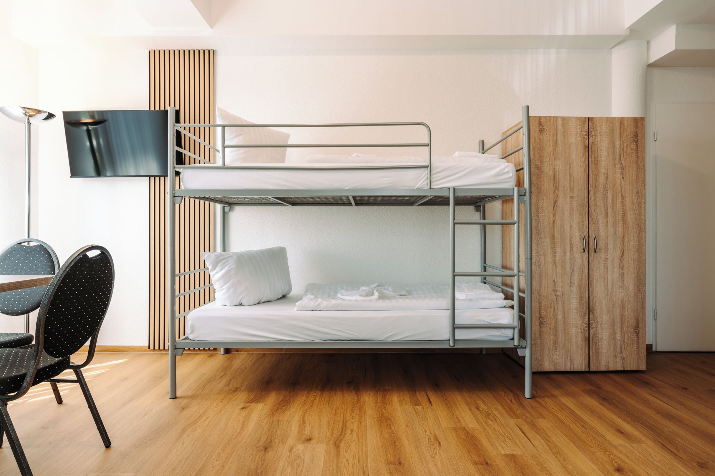 Ein Schlafsaalzimmer mit Etagenbetten, Schreibtisch, Stuhl und einem an der Wand befestigten Fernseher.