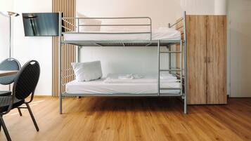 Ein Schlafsaalzimmer mit Etagenbetten, Schreibtisch, Stuhl und einem an der Wand befestigten Fernseher.