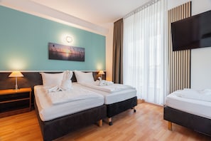 Habitació d'hotel amb dos llits, televisió de pantalla plana, un quadre a la paret i una finestra amb cortines.