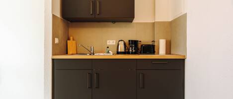A kitchen with dark cabinets, a wooden countertop, and various appliances including a coffee maker and a kettle.