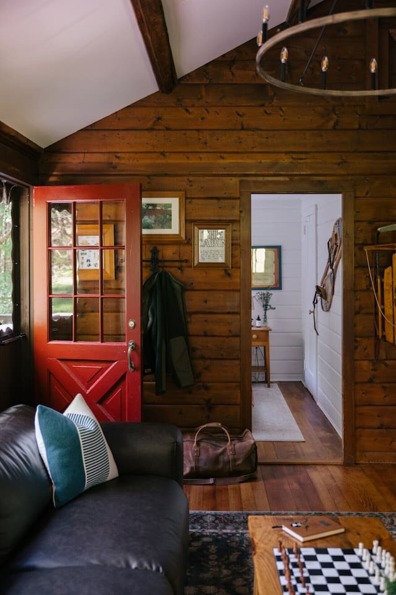 L’intérieur d’un chalet accueillant, avec une porte rouge, un canapé en cuir et un jeu d’échecs posé sur une table en bois.