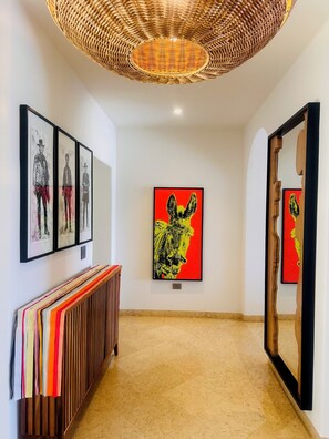A hallway with framed artwork, a woven ceiling light, and a wooden bench.