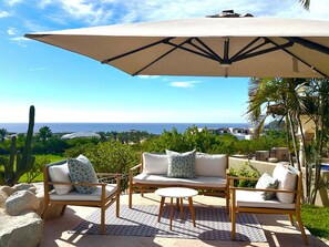 A patio with outdoor furniture, a large umbrella, and a view of the ocean.