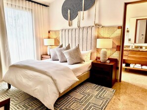 A hotel room with a bed, two bedside tables with lamps, a large mirror, and a view of the bathroom.