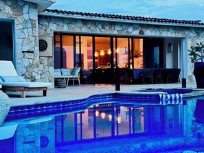 A poolside area with a stone wall, a lounge chair, and a dining area with a table and chairs.