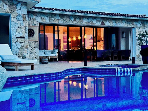 A poolside area with a stone wall, a lounge chair, and a dining area with a table and chairs.