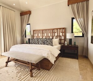 A bedroom with a large bed, wooden headboard, two bedside tables with lamps, and a view of greenery outside.
