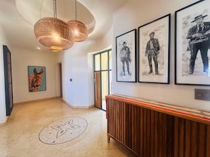 A hallway with framed artwork, a woven light fixture, and a wooden bench.