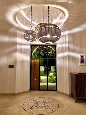 A hallway with a large wooden door, a round carpet with a floral pattern, and three hanging wicker chandeliers.