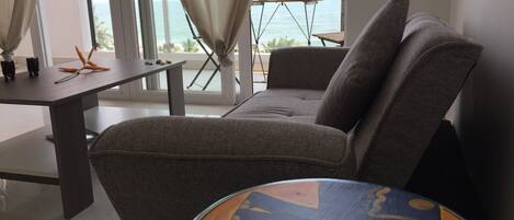 A modern living room with a sofa, a small table, and a view of the sea through large windows.