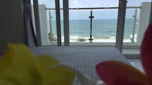 A room with a view of the ocean through large windows, a bed with a patterned bedspread, and a partial view of a yellow and pink object in the foreground. - Wake up to panoramic ocean views from almost every room. (Dehiwala-Mount Lavinia)
