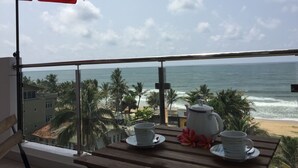 A balcony with a view of the ocean, a table with a teapot, cups, and a red umbrella. - Wake up to panoramic ocean views from almost every room. (Dehiwala-Mount Lavinia)