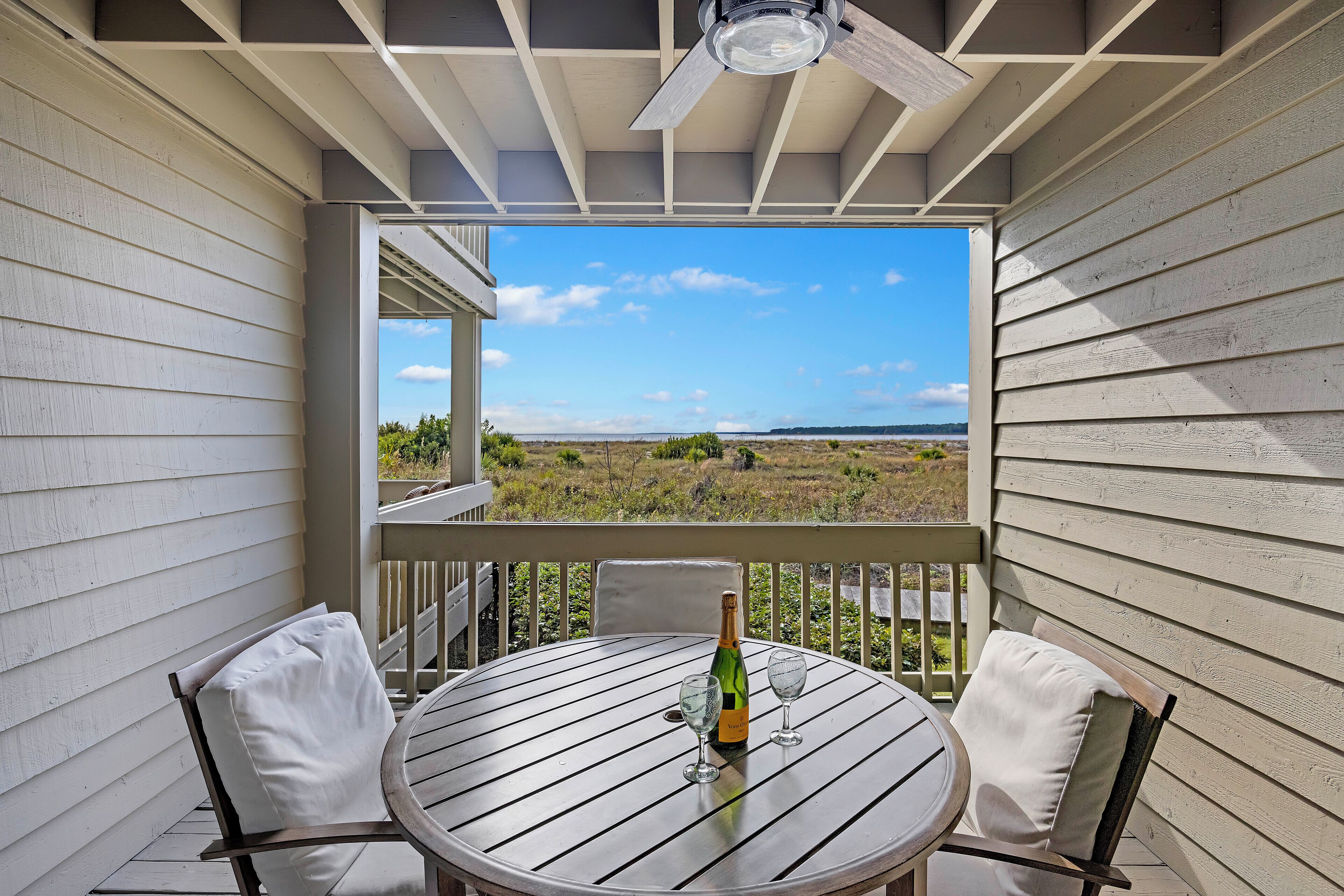 A round table with two chairs, a bottle of champagne, and two glasses on a balcony with a view of the landscape.