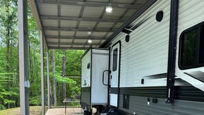 A covered RV with a picnic table and chairs, a blue mat, and a concrete floor. - Charming RV in Lovely Oxford with AC, WiFi (Oxford)