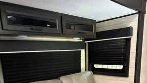 A grey sofa with a red and beige pillow, a black headboard, and a window with blinds. - Charming RV in Lovely Oxford with AC, WiFi (Oxford)
