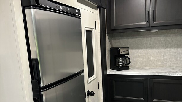 A compact kitchen with a stainless steel refrigerator, a coffee maker, and dark cabinetry. - Charming RV in Lovely Oxford with AC, WiFi (Oxford)