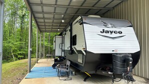 A Jayco RV parked inside a covered garage with a blue mat and a table with chairs outside. - Charming RV in Lovely Oxford with AC, WiFi (Oxford)