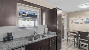 A kitchen with dark wood cabinets, a granite countertop, a double sink, and a window with a view of outdoor furniture.