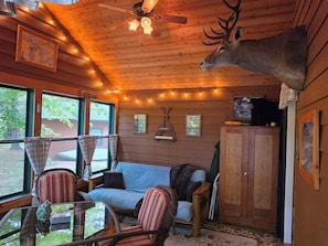 Ein gemütliches Blockhaus-Interieur mit Deckenventilator, Holzwänden, einem aufgehängten Hirschgeweih, einer Couch, Sesseln und einem Tisch.