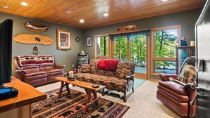 A cozy living room with a fireplace, leather sofas, and a large window offering a view of the outdoors.