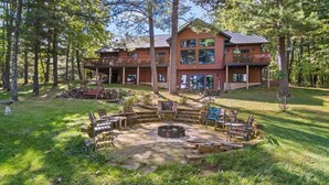 A two-story lodge with a deck and a fire pit area surrounded by outdoor furniture.