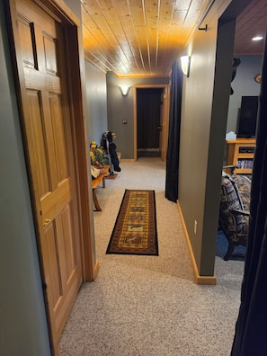 Un couloir avec une porte en bois, un tapis, un banc et un téléviseur à l’arrière-plan.