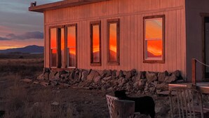 A wooden building with large windows, a stone foundation, and a rustic setting. - Unique and Marvelous Hideaway with the Cosmic Energy of Crestone! (Crestone)