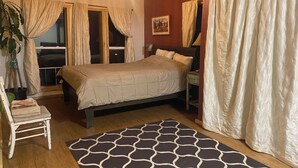 A bedroom with a bed, a nightstand, a chair, a window with curtains, a painting on the wall, and a patterned rug. - Unique and Marvelous Hideaway with the Cosmic Energy of Crestone! (Crestone)