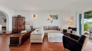 A living room with a sofa, ottoman, and armchairs, a wooden cabinet, and a vase with flowers. - Villa Mesco 360, Terre Marine (Levanto)