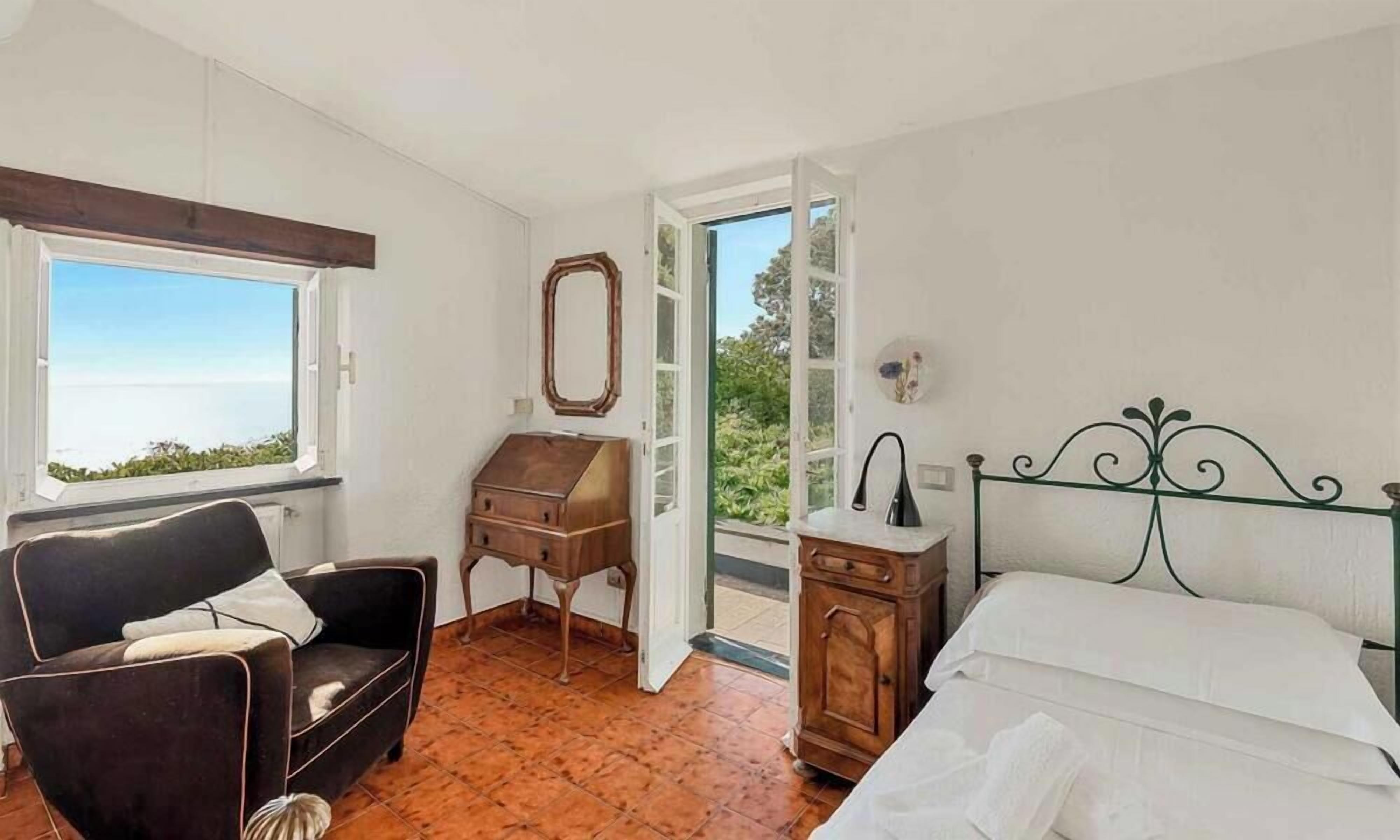 Quarto com cama, uma cadeira, escrivaninha e vista para o exterior.