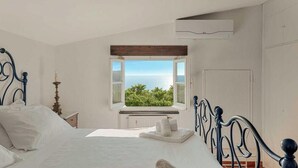 A bedroom with a bed, a window with a view of greenery and the sea, a radiator, and a white wall. - Villa Mesco 360, Terre Marine (Levanto)