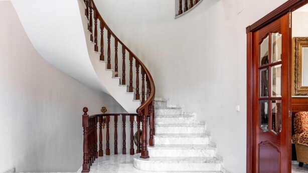 Una escalera de mármol con barandilla de madera que lleva a una puerta con paneles de vidrio.
