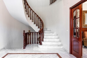 Una escalera de mármol con barandilla de madera que lleva a una puerta con paneles de vidrio.