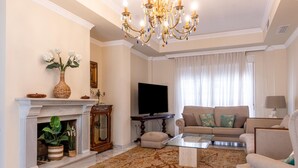 Una sala de estar con chimenea, sofá, televisión y candelabro.