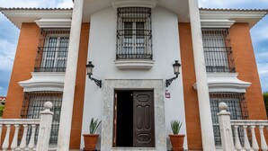 Un edificio con una puerta central grande, dos ventanas con barrotes y un balcón.