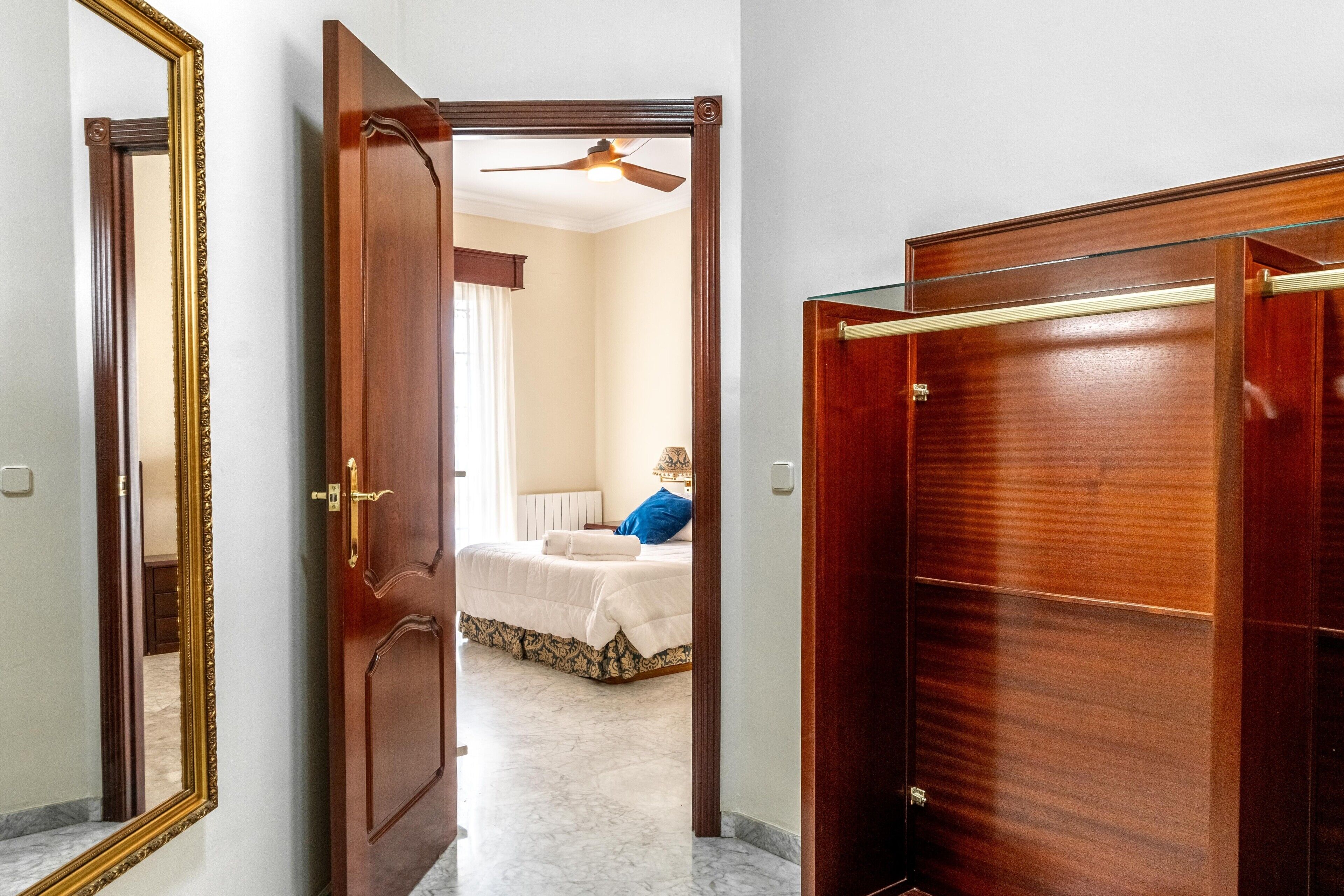 Un couloir avec une porte en bois, un miroir et un lit à l’arrière-plan.