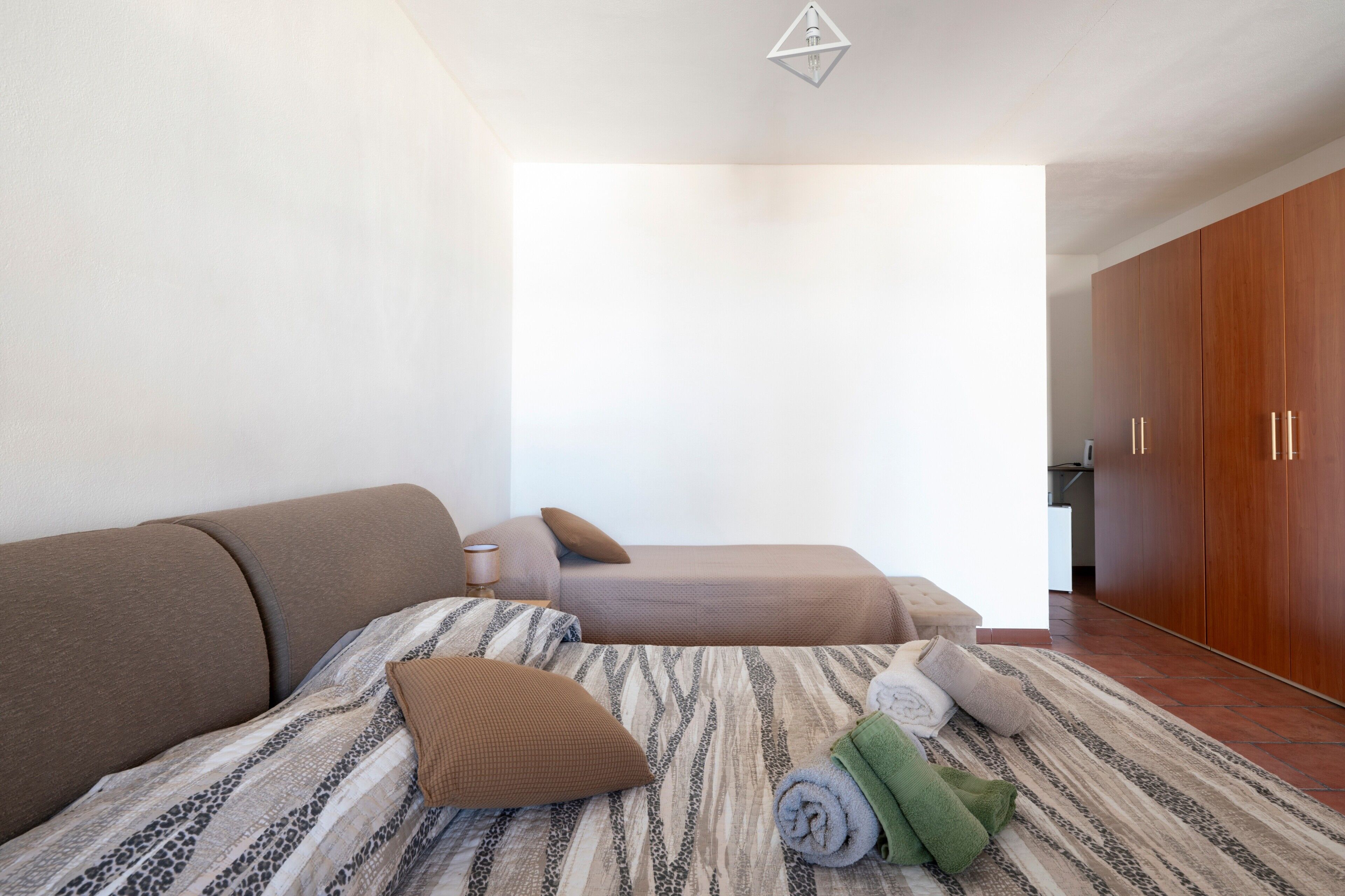A room with a bed, a sofa, a wooden wardrobe, and a window.