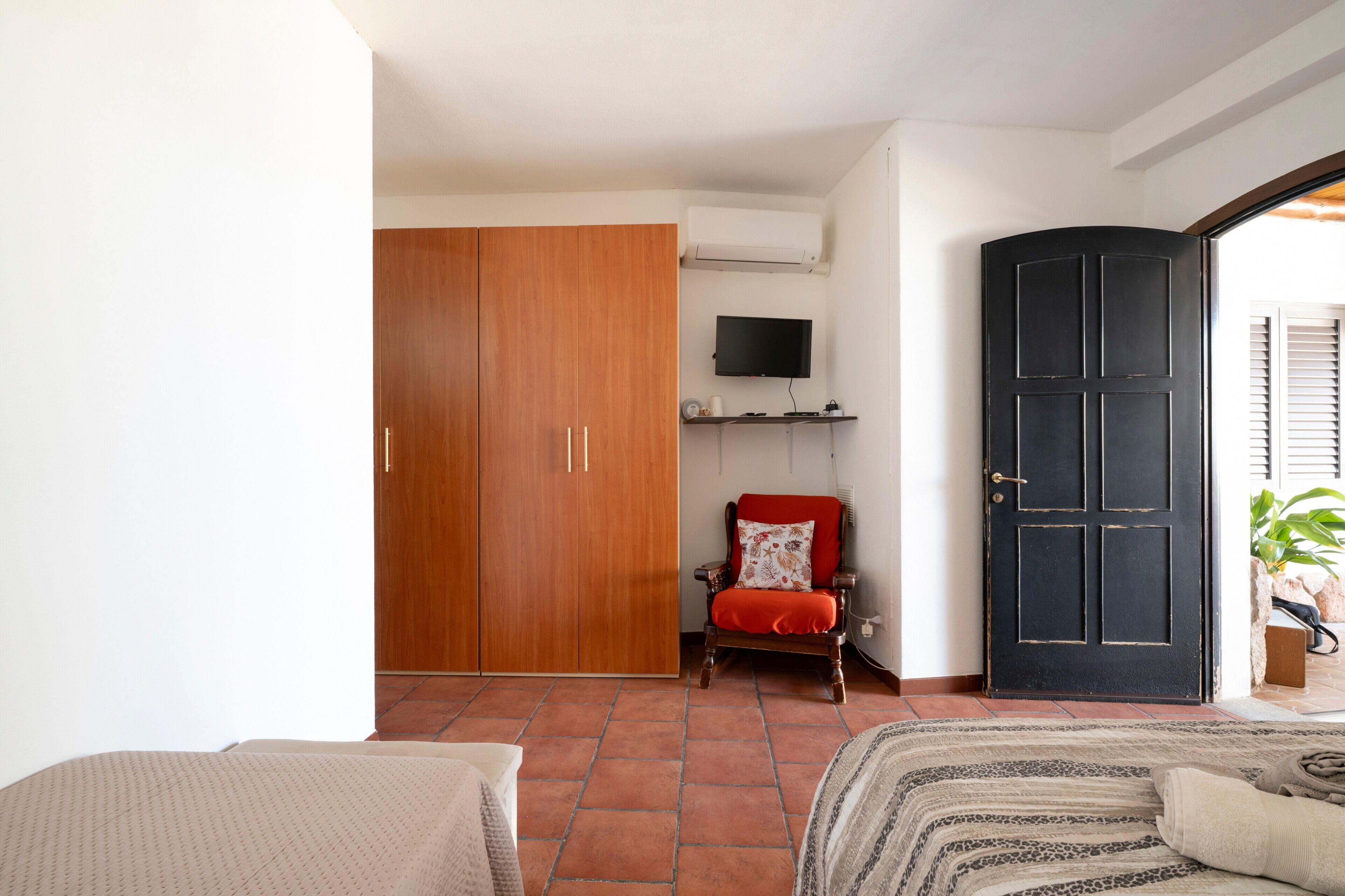 A bedroom with a wardrobe, a television, a door, and a bed.