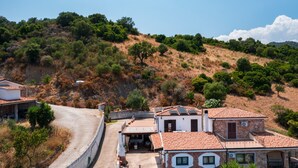 A hillside property with a curved driveway, stone buildings, and a view of the surrounding hills.